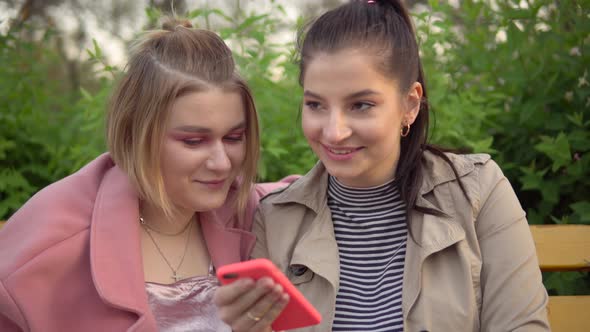 Two Attractive Happy Girls Looking at Phone Screen Laughing Friendship Concept