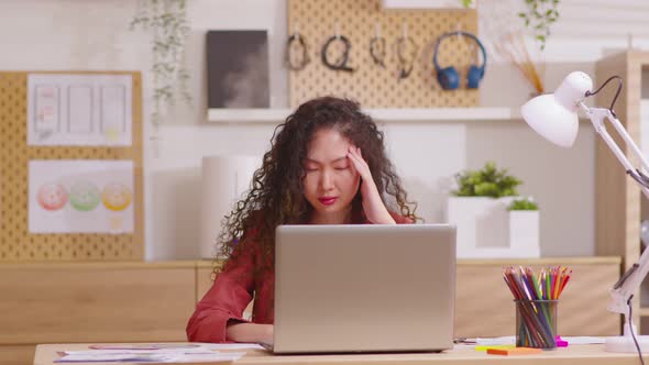Asian woman sitting at desk in front of laptop stressed out face and headache shows her stressful alt