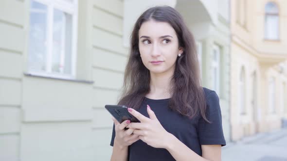A Young Turkish Woman Works on a Smartphone in the Street in an Urban Area alt
