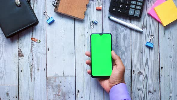 Top View of Man Hand Holding Smart Phone with Empty Screen on Office Desk alt