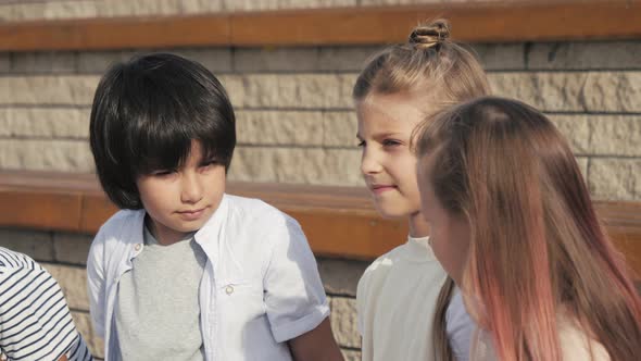 Diverse Group of Kids Sitting on a Bench Together Waiting. alt