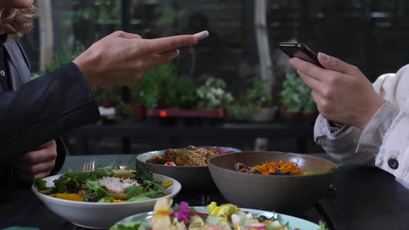 Two Pair of Hands Taking Pictures of Healthy Vegan Meals Served on Black Wooden Table alt