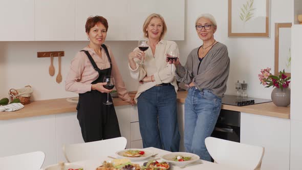 Portrait of Three Elegant Women with Glasses of Wine at Kitchen alt