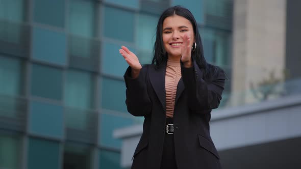 Young Successful Smiling Hispanic Business Woman Clapping Hands on Background Office Building alt