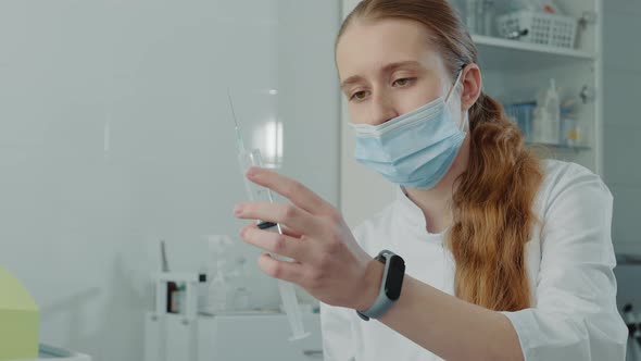 Young Nurse Trainee Holding a Large Syringe with Medicine and Examining a Syringe alt