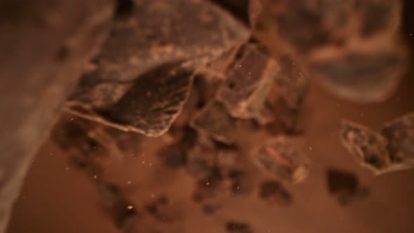 Super Slow Motion Detail Shot of Falling Raw Chocolate Chunks on Brown Background at 1000Fps alt