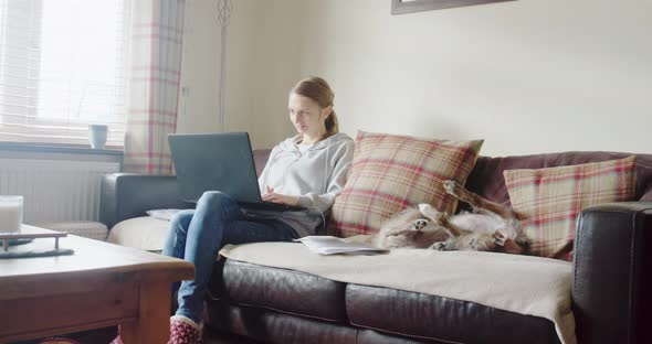 WS Woman using laptop on sofa, dog lying next to her / Staffordshire, UK