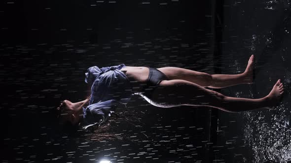 Beautiful girl in a black swimsuit and shirt stands in the rain, enjoys the drops of water, straight alt
