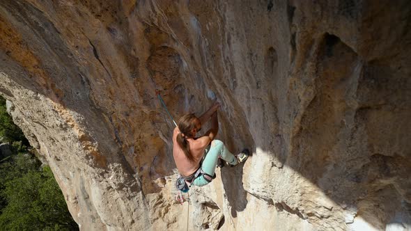 Young Powerful Athletic Man Rock Climber With Long Hair Climbing On Overhanging Cliff By