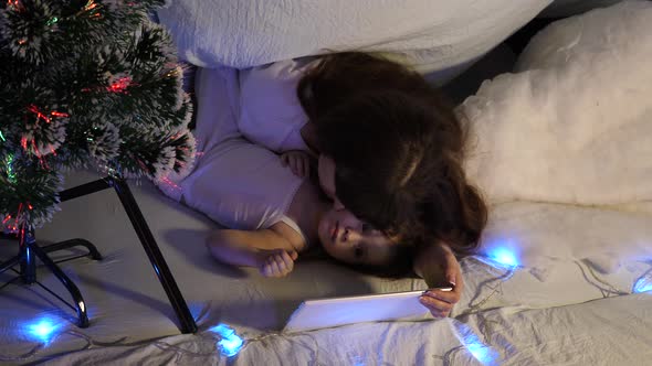 Child and Mother Are Playing with Tablet Computer in Room. Concept of a Happy Childhood and Family alt