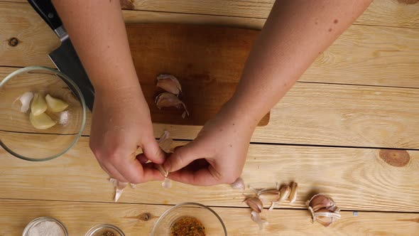 Top view of a woman's hands on a cutting board crushing garlic cloves with a large knife alt