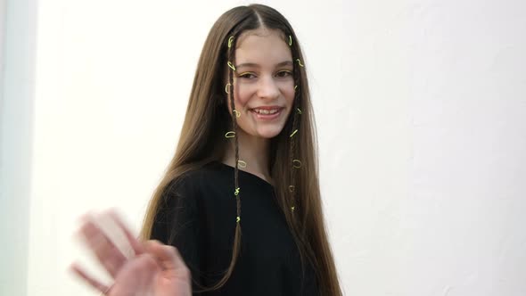 European Teen Girl Waves Her Hand at the Camera She is on a White Background alt