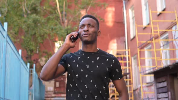 A young smiling black guy is walking down the street and talking on the phone alt