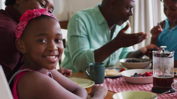 Portrait of african american girl smiling while having breakfast together with her family at home alt