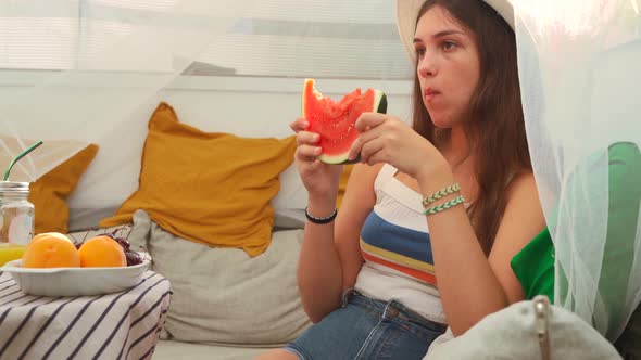 Young woman eating fresh watermelon in backyard tent alt