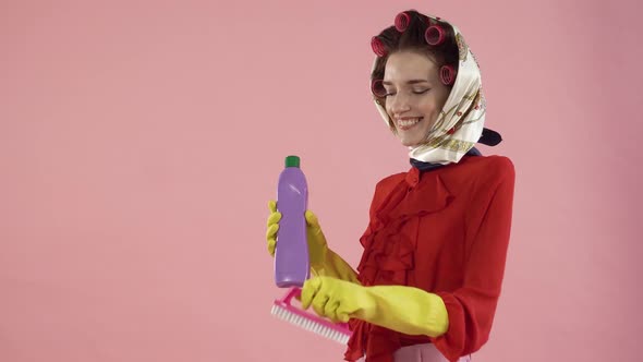 A Woman in a Blouse and Hair Curlers Brushes Her Hair with a Pink Brush Smiles