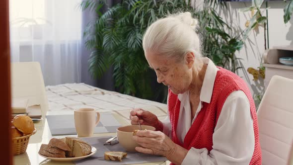 Elderly Woman Eating Soup and Bread at Home