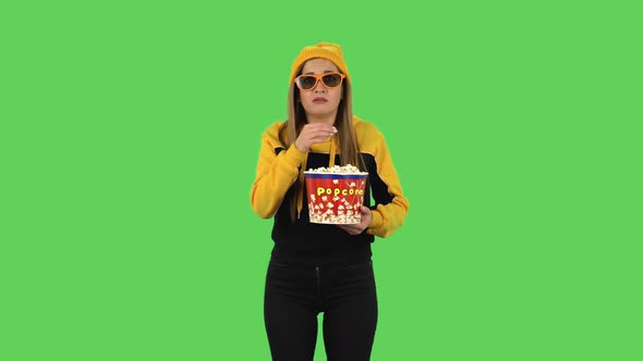 Modern Girl in Yellow Hat in 3D Glasses Is Watching a Scary Movie and Eating Popcorn. Green Screen alt
