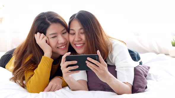 Young Asian lesbian couple selfie on a smartphone in a bedroom at home.