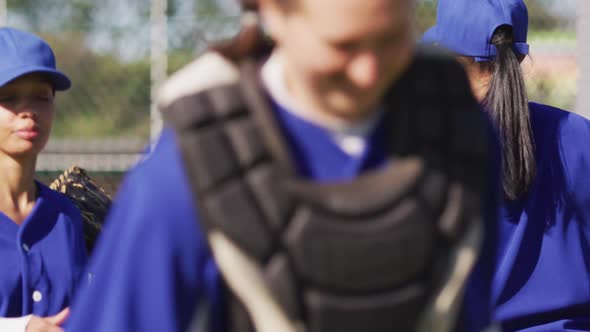 Happy diverse group of female baseball players smiling and banging gloves after game alt