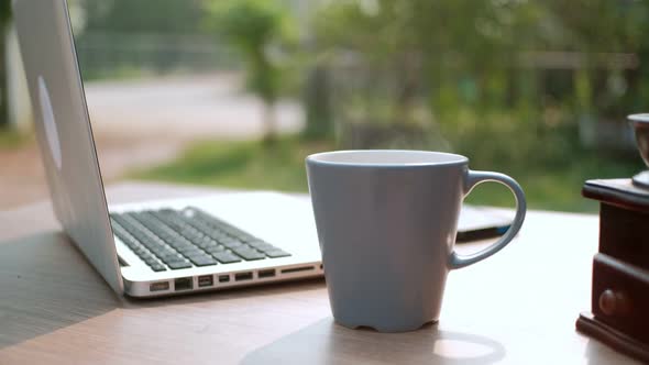 Close up Cup of coffee, coffee with smoke on desk table with laptop computer background in morning. alt