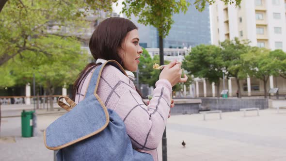 Young Caucasian woman eating and walking alt