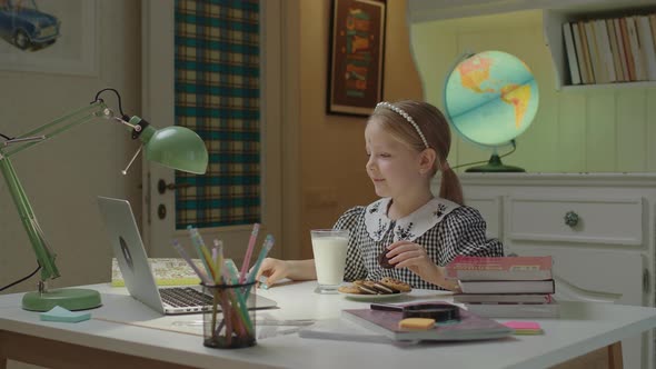 Happy Schoolgirl Talking Online with Friends Eating Cookies and Drinking Milk alt