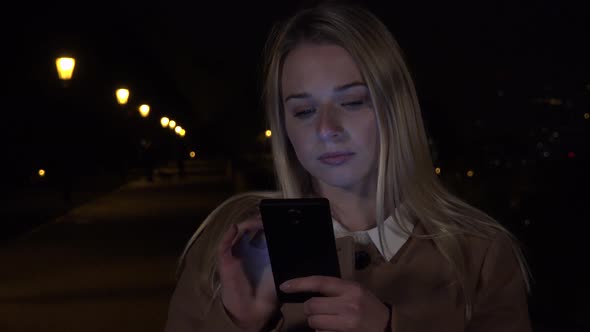 A Young Beautiful Woman Works on a Smartphone in an Urban Area at Night alt