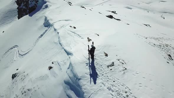 Aerial drone circling view of a skier with skis on top of a snow covered mountains in the winter. alt