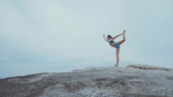 Woman Standing on One Leg and Meditating on Rocks Near Ocean alt