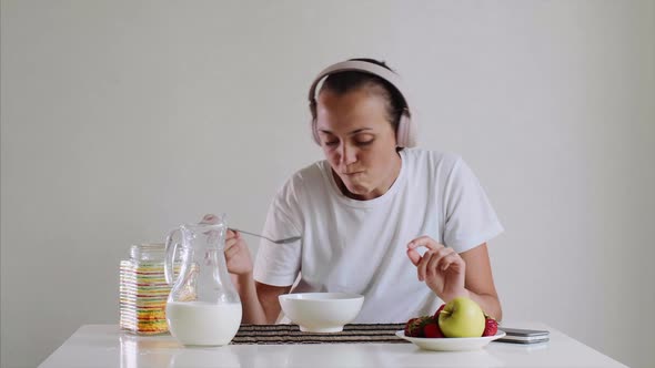 Woman in headphones is listening music while eating cornflakes with milk.