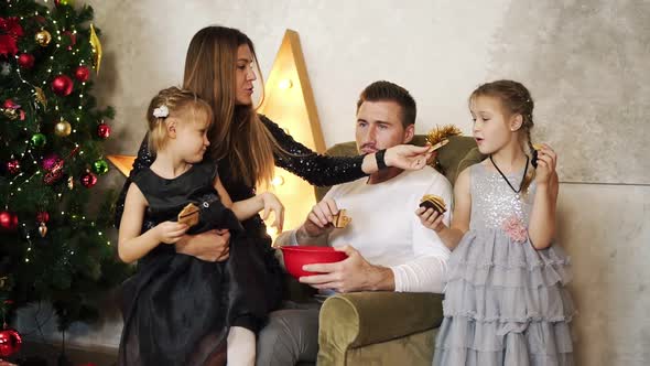 Happy Family of Four Sitting By the Christmas Tree and Eating Chocolate Cookies alt