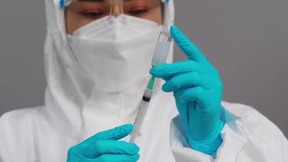 doctor in protective PPE suit drawing vaccine bottle into syringe injection medicine