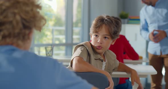 Back View of Schoolboy Sitting at Desk on Exam and Turn Around Talking to Classmate alt