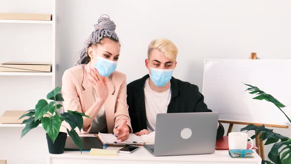 Business conference online. Young modern woman and man in medical masks communicate using laptop