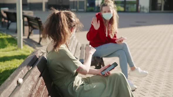 Two Familiar Young Girls Greet Each Other By Waving at Hand at a Safe Social Distance. They