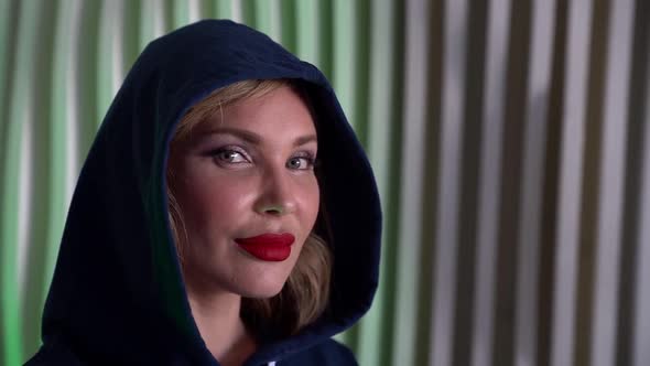 Portrait of a Middleaged Blonde with Red Lipstick on Lips and a Blue Hood Against a Striped Wall alt