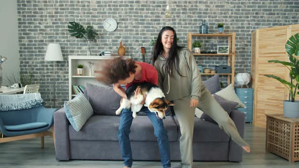 Joyful Guy Dancing with Girlfriend Holding Corgi Puppy Having Fun at Home alt