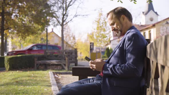 A Middleaged Handsome Caucasian Man Pulls Out a Smartphone and Works on It