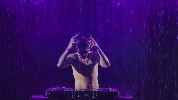A Sexy Male Dj with a Shiny Body From the Rain Plays on the Remote Control for Mixing Music in a alt