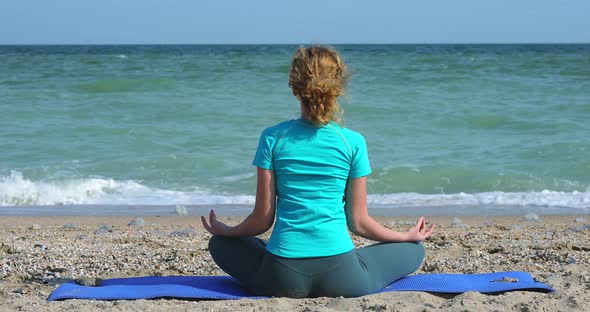 Young Woman Meditates on the Shore of the Ocean
