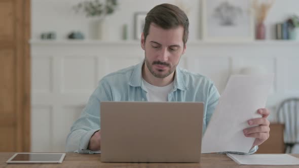 Young Man Doing Paperwork on Laptop in Office alt