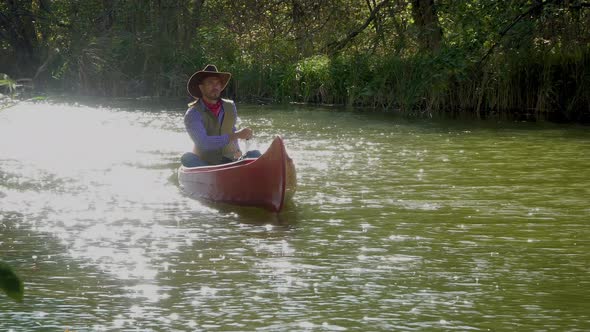 Cowboy in a Canoe Floats on the River in the Forest alt