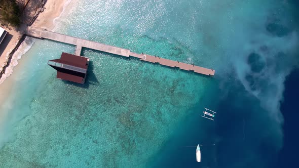 Epic aerial top down of crystal clear coral reefs under wooden pier on Gili Meno Island during sunsh alt
