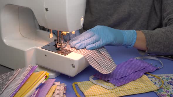 Woman in gloves sew reusable cloth protective face mask with sewing machine at home alt