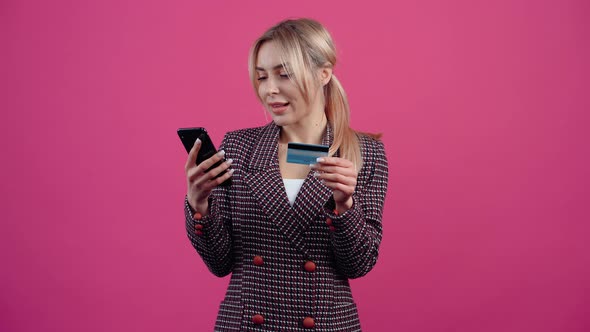 The Cheerful Young Woman with Her Phone in Her Hand and Her Shopping Card is Shopping Online Happy alt