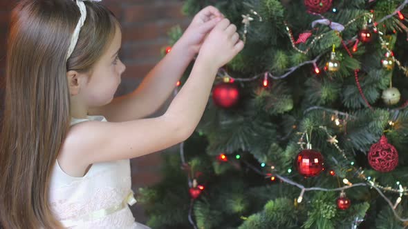 little girl in a beautiful dress decorates a Christmas tree