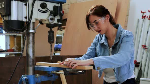 Asian carpenter student woman mark on wood before drill by drilling machine in university workshop