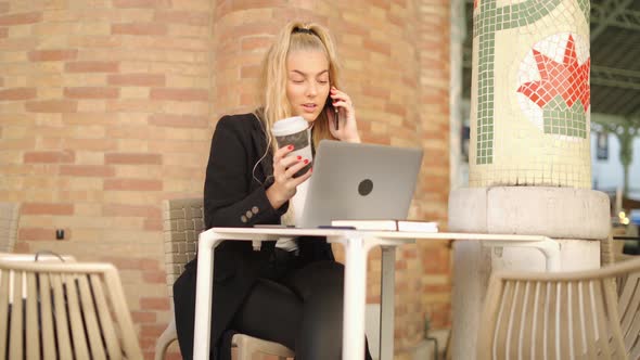 Woman talking on smartphone while working with laptop in cafe alt