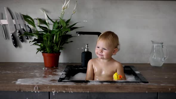 Cute Happy Baby Girl with Playing with Water and Foam in a Kitchen Sink at Home alt